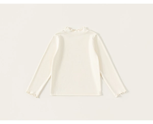Close-up of cream knit shirt showing ruffled collar and soft cotton texture detail