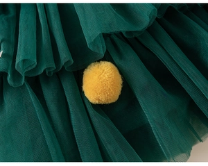 Detail of multi-layer dark green tulle fabric and a yellow pom-pom on kids clothing