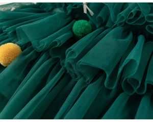 Detail of dark green layered tulle with colorful pom-pom ornaments on a girl's garment