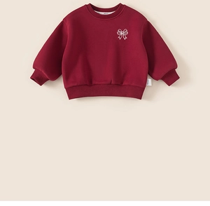 Détail d'un sweat en polaire rouge avec broderie nœud blanc et poignets côtelés