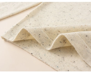 Close-up of off-white confetti knit fabric with soft texture and ribbed edge detail