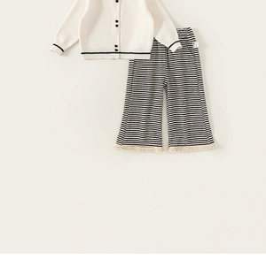 Detailansicht der cremefarbenen Strickjacke mit Herzknöpfen und gestreifter Hose für Mädchen