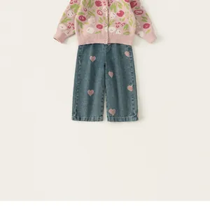 Detail der rosa geblümten Strickjacke und blauen Weitbeinhose mit Herzstickerei