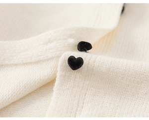 Detail eines weißen Strick-Cardigans mit schwarzen Herzknöpfen und weicher Stoffstruktur