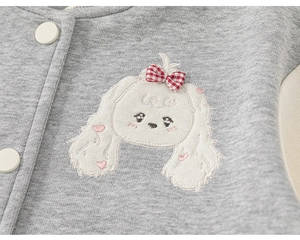 Détail de veste en tricot grise pour enfant avec broderie de chien et bouton blanc mat