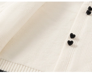 Detailansicht der cremefarbenen Strickjacke mit schwarzen Herzen und Rippbündchen