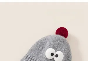 Detailed knit texture of grey baby winter hat with large cartoon eyes and red pompom