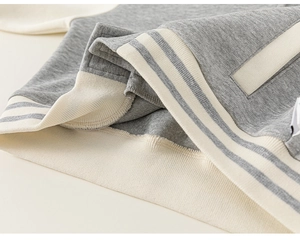 Détail du tissu tricoté gris et des poignets rayés crème sur veste baseball enfant