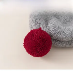 Detailed view of gray chunky knit texture and vibrant red contrast pom-pom on baby hat