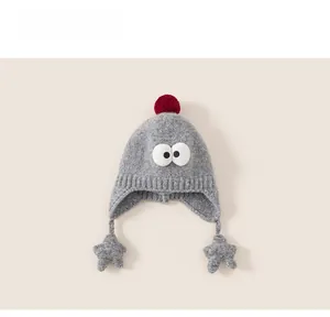 Close-up of gray knit baby earflap hat with red pompom and cartoon big eyes decor