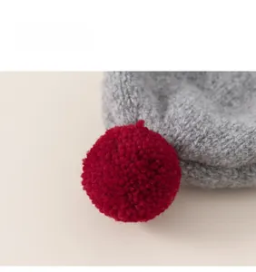 Close-up of a grey knitted baby hat with a vibrant red fluffy pom-pom detail