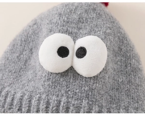 Detailed knit texture of a grey children's hat with cartoon eyes and red pom-pom