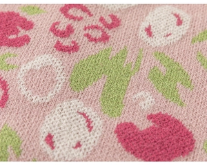 Makroaufnahme von kirschrosa Strickstoff mit weißen Smileys und Jacquard-Blumenmustern