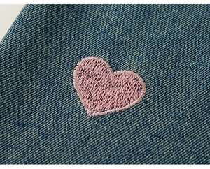 Nahaufnahme der rosa Herzstickerei auf hochwertigem blauem Denim für Kinderkleidung
