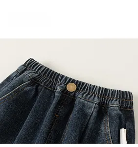 Detail of elastic waist with bronze button and orange stitching on blue denim jeans