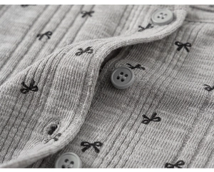 Détail du tricot côtelé gris avec motifs nœuds noirs et boutons assortis sur le haut