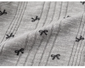Détail macro du tricot côtelé gris avec motifs de nœuds noirs brodés sur le gilet
