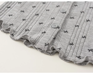 Détail du tricot gris côtelé avec motifs nœuds noirs et bordure ondulée douce