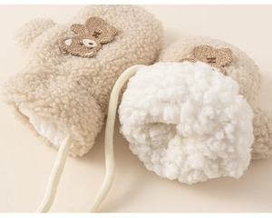 Detailed macro view of beige faux shearling kids mittens with cute bear embroidery and lanyard