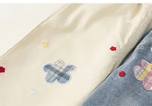 Detalle de bordado de cuadros coloridos en pantalones infantiles de sarga y denim