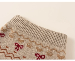 Detail of soft beige knitwear with red bow and brown paw patterns on ribbed fabric