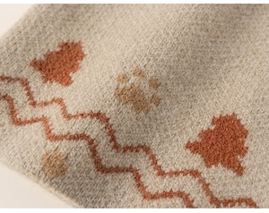 Detailed close-up of soft beige knit fabric featuring orange and brown jacquard tree patterns