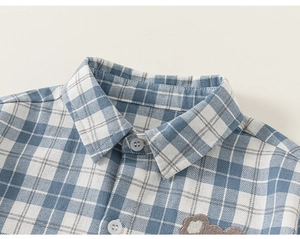 Detail of boys' blue plaid shirt with classic collar, small buttons and bear patch embroidery