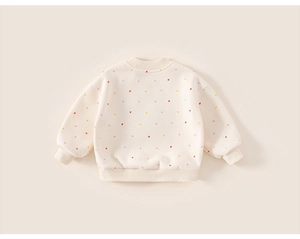 Close-up of cream sweatshirt featuring colorful heart patterns and ribbed cuffs detail