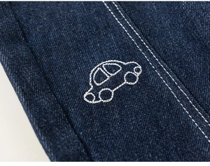 Detailed close-up of dark blue denim fabric featuring white car outline embroidery and stitching