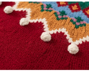 Gros plan sur un pull en tricot rouge avec motifs à vagues et détails de pompons blancs