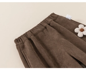Detail of dark brown corduroy girl trousers with elastic waist and 3D floral accent