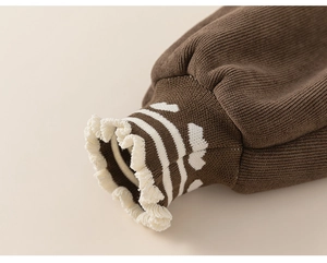 Gros plan de poignets en tricot marron avec motifs cœurs blancs et bords à volants