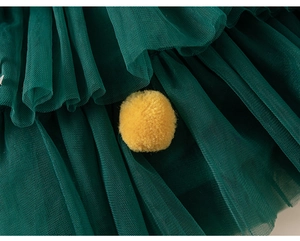 Détail des couches de tulle vert foncé sur un tutu avec une décoration pompon en peluche jaune