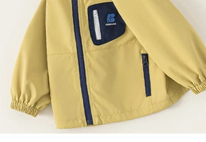 Détail du coupe-vent enfant avec tissu jaune gingembre et poche contrastée marine