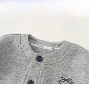Detail of grey knitted kids cardigan showing round neck with navy button and bow embroidery