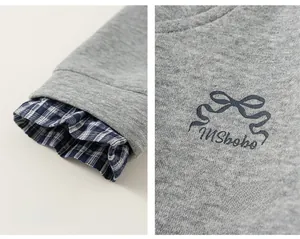 Detail of gray knit sweater featuring plaid patchwork cuffs and a bow ribbon print