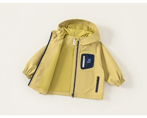 Détail de la veste coupe-vent pour enfant avec poche contrastée et tissu mat jaune