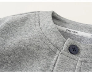 Detail of grey knitted fabric texture and button on children's plaid patchwork jacket