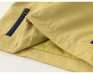 Détail de l'ourlet de veste jaune clair avec poche zippée bleu marine et tissu tissé