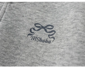 Macro detail of girls' grey knit jacket featuring a ribbon bow and INSbobo logo