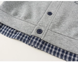 Detail view of gray knit sweater with blue plaid shirt hem and matte buttons