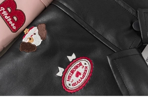 Detailed view of child's faux leather jacket with embroidered cartoon dog and heart patches
