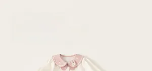 Detail of baby girls cream top featuring pink Peter Pan collar with rabbit doll and floral embroidery