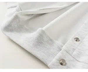 Macro detail of elastic ribbed hem and metal snap buttons on grey baseball jacket