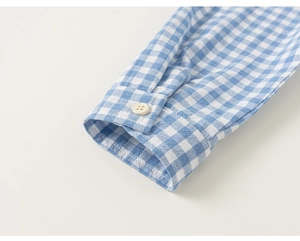 Detail of blue and white gingham shirt cuff with a single button and fine stitching
