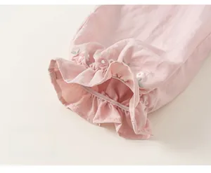 Close-up of pink cotton trousers featuring elastic ruffle hems and floral embroidery