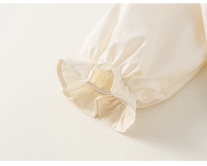 Detail shot of ruffled elastic cuffs on cream white long sleeve girl's cotton blouse