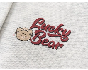 Detail of grey knit fabric showing a screen-printed brown cartoon bear and Lucky Bear text