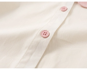 Detailed close-up of cream white fabric texture with light pink buttons and collar trim