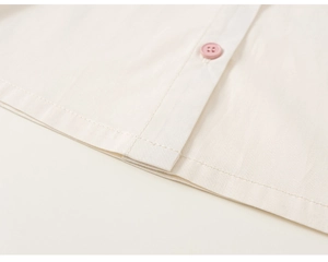 Close-up of pink button and stitching on beige cotton fabric for kids outfit